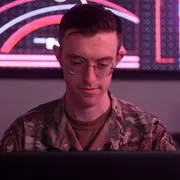 A member of the US military working on a computer in dim light.