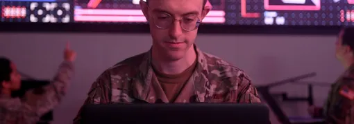 A member of the US military working on a computer in dim light.