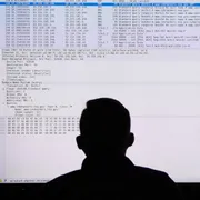 Two US Coast Guard personnel participate in a cybersecurity exercise in front of a large monitor.